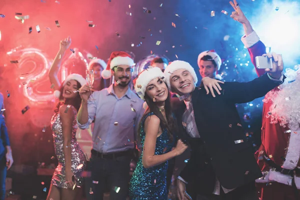 Pareja joven divirtiéndose en la fiesta de Año Nuevo. Hacen selfie en un teléfono inteligente . — Foto de Stock