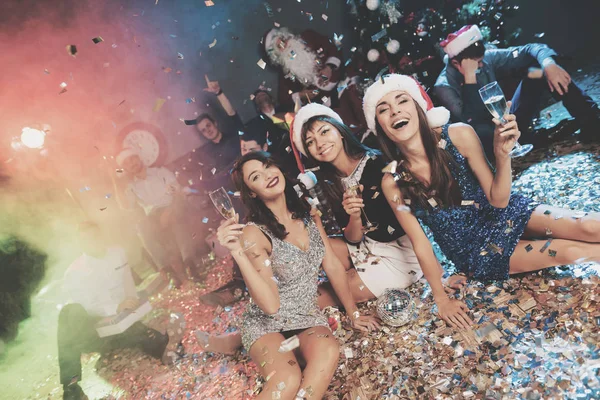 Trois filles dans de belles robes de soirée sont assises sur le sol avec des verres de champagne dans leurs mains . — Photo