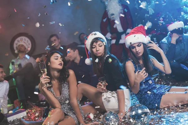 Tre ragazze con bei vestiti da sera sono sedute sul pavimento con bicchieri di champagne in mano . — Foto Stock
