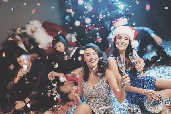 Dos chicas están sentadas en el suelo. Alrededor de ellos hay confeti disperso. Descansan después de la fiesta para el nuevo año —  Fotos de Stock