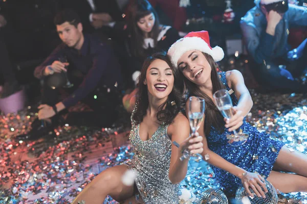 Duas raparigas estão sentadas no chão. Em torno deles está espalhado confete. Eles descansam após a festa para o ano novo — Fotografia de Stock