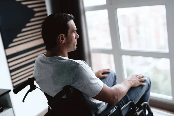 Инвалид в инвалидной коляске сидит перед большим панорамным окном и смотрит в него . — стоковое фото