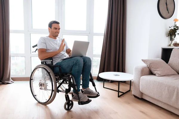 De gehandicapte persoon zit in een rolstoel. Hij heeft een laptop op schoot, waarvoor hij werkt. — Stockfoto