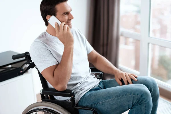 Der Behinderte sitzt im Rollstuhl. Er spricht mit jemandem auf seinem Smartphone. er lächelt. — Stockfoto