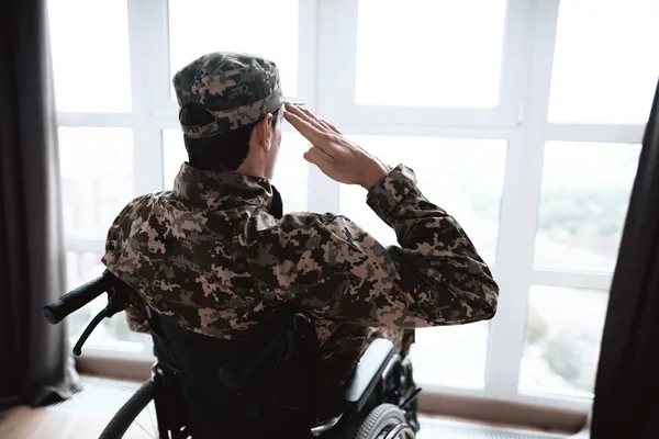 Інваліди у військовій формі сидять у інвалідному візку. Він дивиться у вікно і салюти . — стокове фото