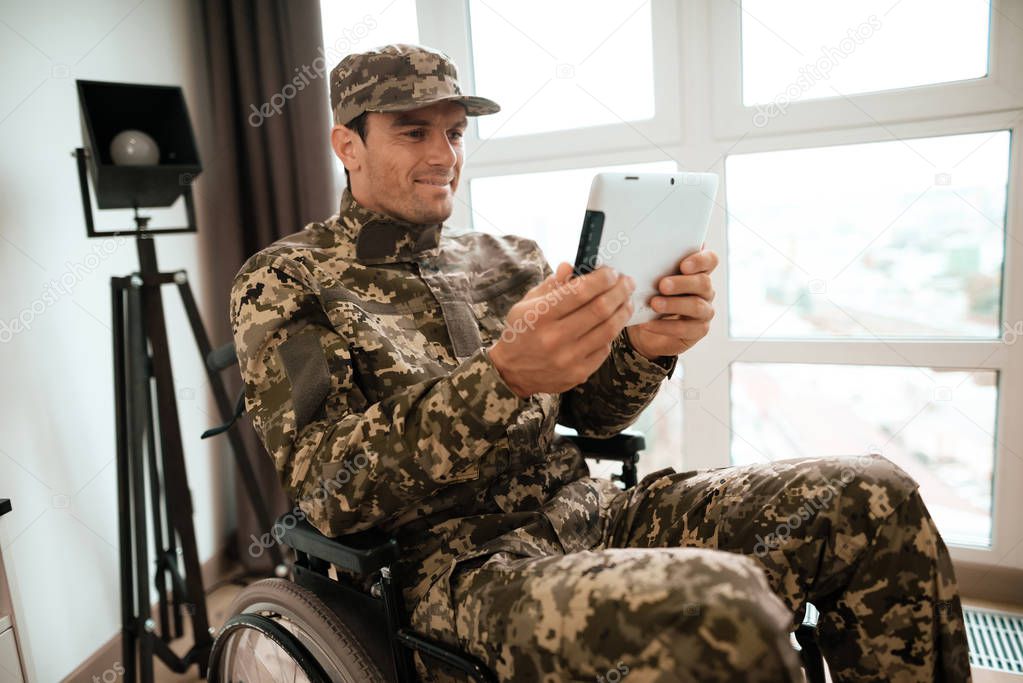 The disabled in military uniform sits in a wheelchair and communicates with someone through a tablet.