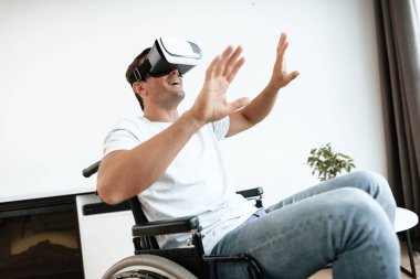 Engelli kişi sanal gerçeklik bardaklarda tekerlekli sandalyede oturuyor. O ellerini yanlara yaymak.