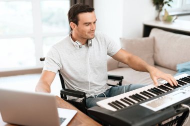 Engelli kişi önünde synthesizer tekerlekli sandalyede oturuyor. müzik yazıyor. Yakında onun gri laptop olduğunu.