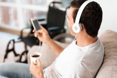Engelli kişi koltukta oturuyor. O müziği dinliyor ve onun smartphone ekranında görünüyor.