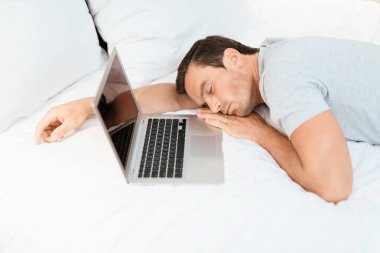Belgili tanımlık laptop üzerinde ve açık dönüşmeden adam bir uyku yatağa düştü. Gri bir T-shirt giyiyor.