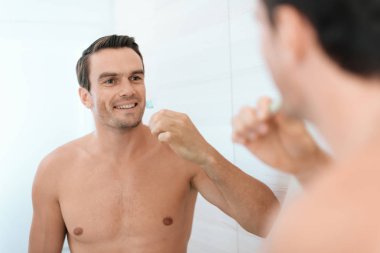 Bir adam sabah tuvalette ayakta ve Dişlerini fırçalıyor. O gülümsüyor.