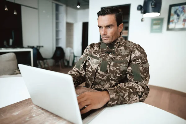 Désactivé en uniforme militaire, il travaille pour son ordinateur portable. Il est assis à son bureau. . — Photo