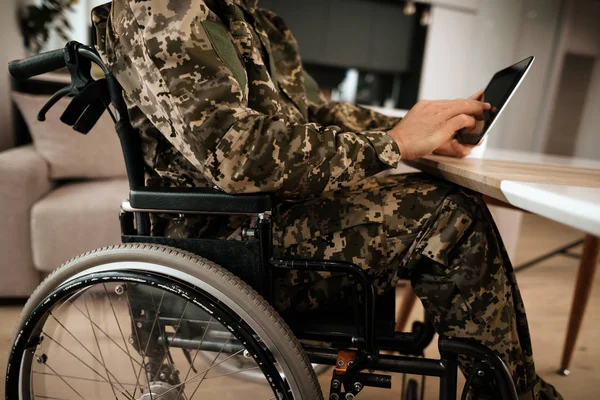Niepełnosprawnych w wojskowym mundurze, czytając coś na jego nowoczesny tablet. Za to duże panoramiczne okna. — Zdjęcie stockowe