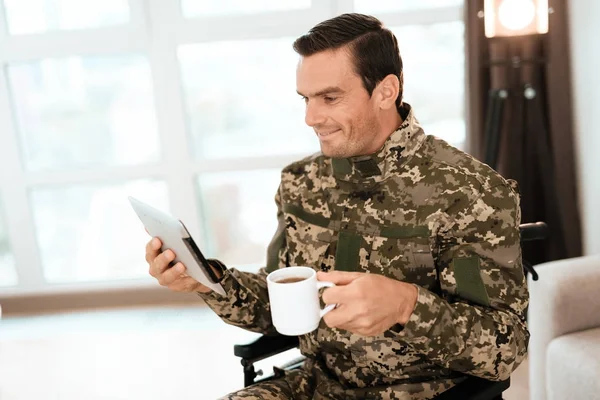 Los discapacitados en uniforme, leyendo algo en su tableta moderna y tomando café . — Foto de Stock