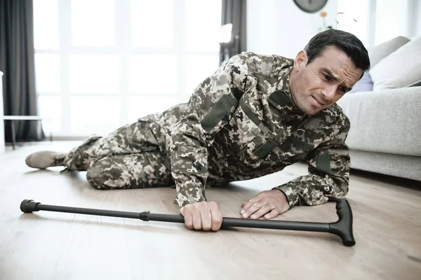 Ein Mann in Uniform liegt auf dem Boden. Er fiel mit einer Krücke in der Hand. Es tut weh. — Stockfoto