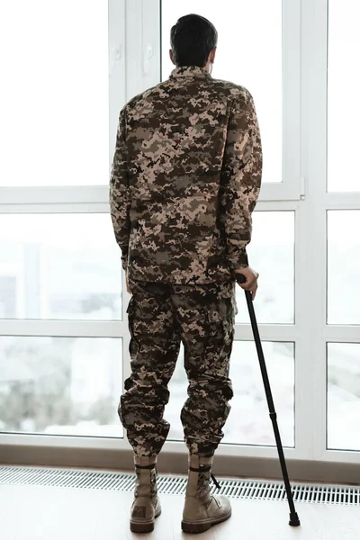 Солдат з обмеженими можливостями спирається на череп біля вікна. Він дивиться у велике панорамне вікно . — стокове фото