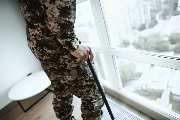 A disabled soldier stands with his hand on the window. He feels sad and depressed. — Stock Photo, Image