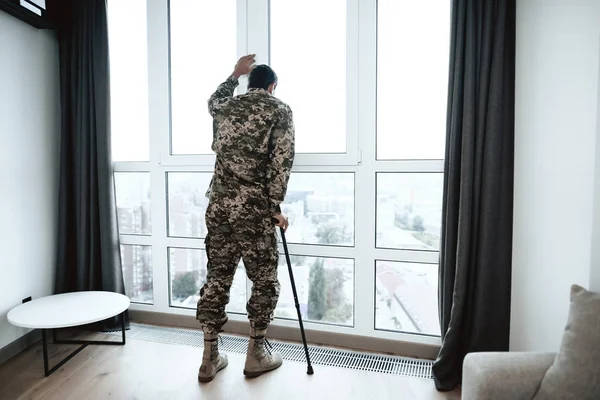 Солдат-інвалід стоїть з рукою на вікні. Він відчуває себе сумним і пригніченим . — стокове фото
