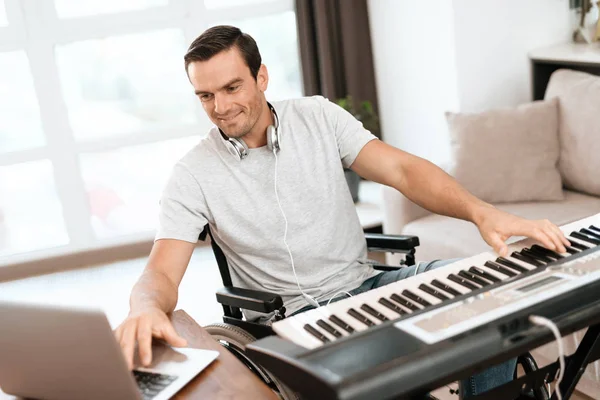 The disabled person is sitting in a wheelchair in front of the synthesizer. writes music. Nearby is his gray laptop. — Stock Photo, Image