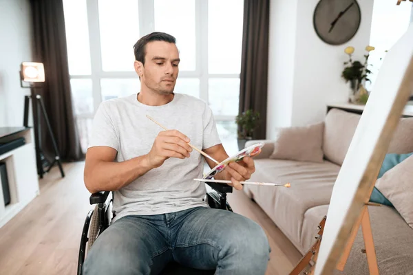 La persona con discapacidad está sentada en una silla de ruedas frente al caballete. Él dibuja un cuadro . — Foto de Stock