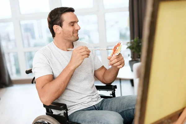 Инвалид сидит в инвалидной коляске напротив мольберта. Он рисует картину. . — стоковое фото