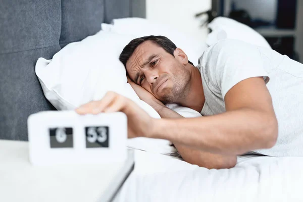 Postižená osoba spí v posteli bílé. Tam je také budík před ním. Mračí a vytáhne ho. — Stock fotografie