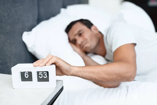 El discapacitado duerme en su cama blanca. Hay un despertador frente a él. Frunce el ceño y lo saca . — Foto de Stock