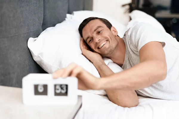 El discapacitado duerme en su cama blanca. Hay un despertador frente a él. Sonríe y lo saca. . — Foto de Stock
