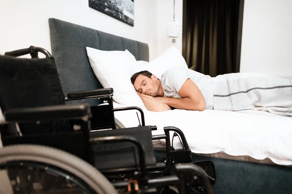 The disabled person sleeps. In the foreground is his black wheelchair. — Stock Photo, Image