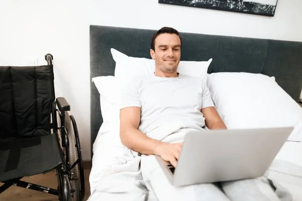Los discapacitados están acostados en la cama y trabajando con un ordenador portátil. Se acaba de despertar. . — Foto de Stock