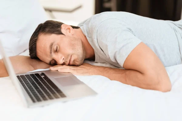 El hombre se quedó dormido en la cama antes de que el portátil estuviera encendido y abierto. Lleva una camiseta gris. . —  Fotos de Stock