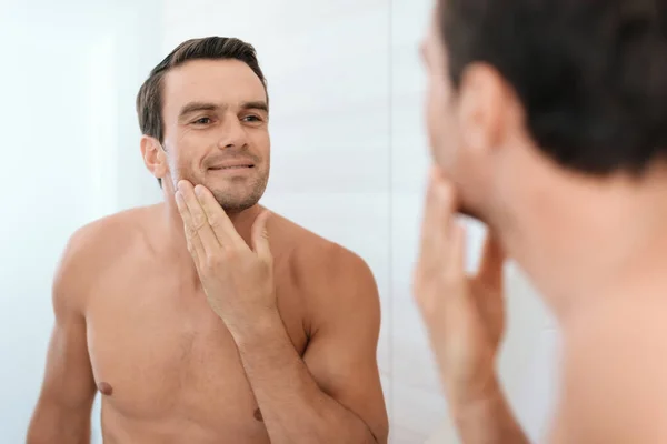 Um homem na casa de banho de manhã. Ele rapa o barbeador elétrico na frente do espelho . — Fotografia de Stock