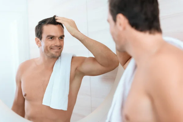 Un hombre se para en el baño por la mañana y se mira en el espejo. Sonríe. . —  Fotos de Stock