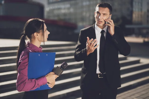 A man in a black suit is telling something on the phone while a journalist looks at him — Stock Photo, Image