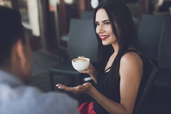 The girl smiles and holds a mug of cappuccino in her hand — Stock Photo, Image