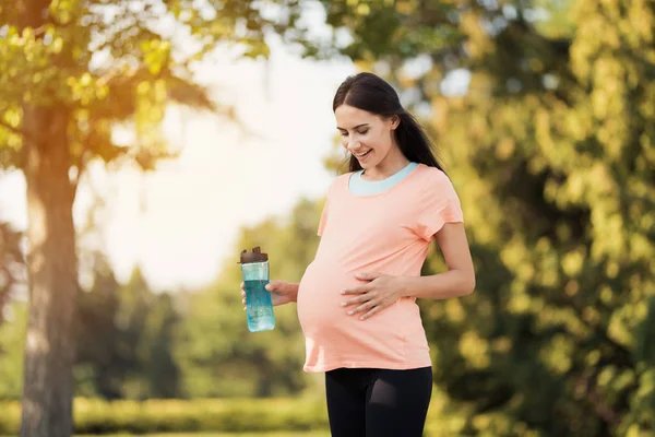 Беременная женщина, гуляющая в парке со спортивной бутылкой в руках — стоковое фото