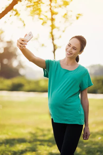 Gravid kvinna gör selfie i parken på sin smartphone — Stockfoto