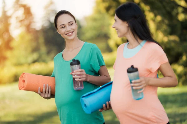 Dos mujeres están de pie en un parque con colchonetas de yoga y botellas deportivas —  Fotos de Stock