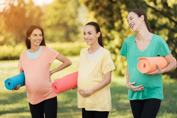 Tre gravida tjejer poserar i en park med yogamattor i hand. De ler och ha kul — Stockfoto