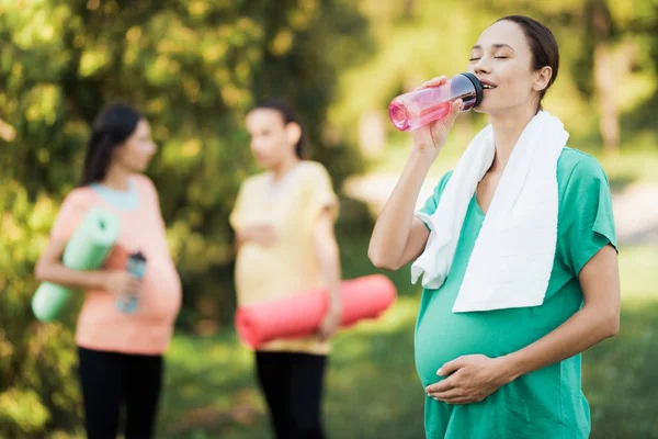 Tre gravida tjejer kom till parken på fitness. En flicka i en grön T-shirt poserar med en sport flaska — Stockfoto