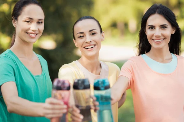 Tres chicas posando en el parque levantando las manos con botellas deportivas —  Fotos de Stock