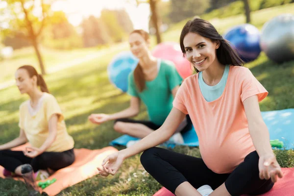 Graviditet yoga. Tre kvinnor sitter på yogamattor i en lotus pose och leende — Stockfoto