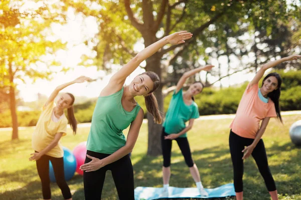 Ioga de gravidez. Três mulheres grávidas de pé no parque e fazendo exercícios. Em conjunto com eles o seu treinador — Fotografia de Stock