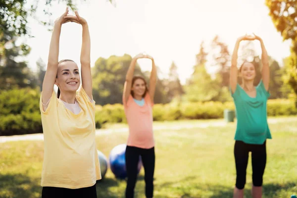 Graviditet yoga. Tre gravida kvinnor står i parken och gör övningar — Stockfoto