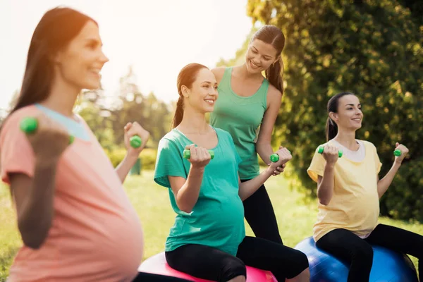 Вагітність йога. Три вагітні жінки займаються фітнесом в парку. Вони сидять на яйцях для йоги — стокове фото