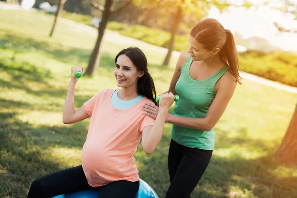 Pregnancy yoga. A coach helps a pregnant woman to do exercises on a ball for yoga