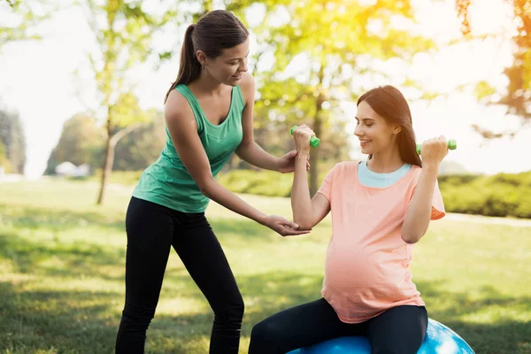 Вагітність йога. Тренер допомагає вагітній жінці робити вправи на м'яч для йоги — стокове фото