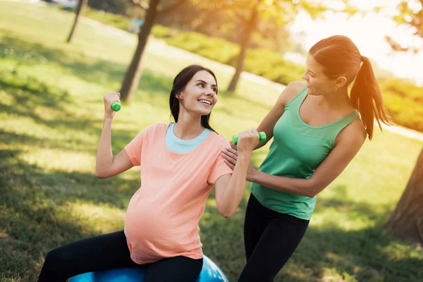 Graviditet yoga. En coach hjälper en gravid kvinna att göra övningar på en boll för yoga — Stockfoto