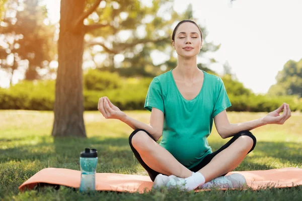 Schwangerschaftsyoga. Eine schwangere Frau im grünen T-Shirt sitzt in Lotus-Pose auf einem Teppich für Yoga — Stockfoto