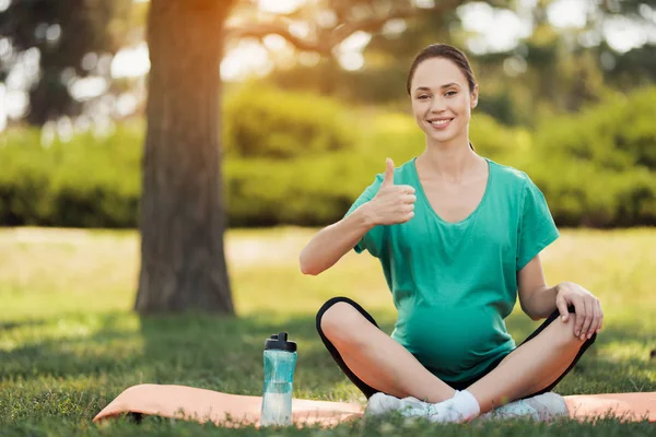 Graviditet yoga. En gravid kvinna i en grön T-shirt sitter i en lotus pose på en matta för yoga — Stockfoto